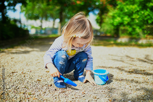 Adorable toddler girl playing with bucket and shovel, making mudpies and gathering small stones photo