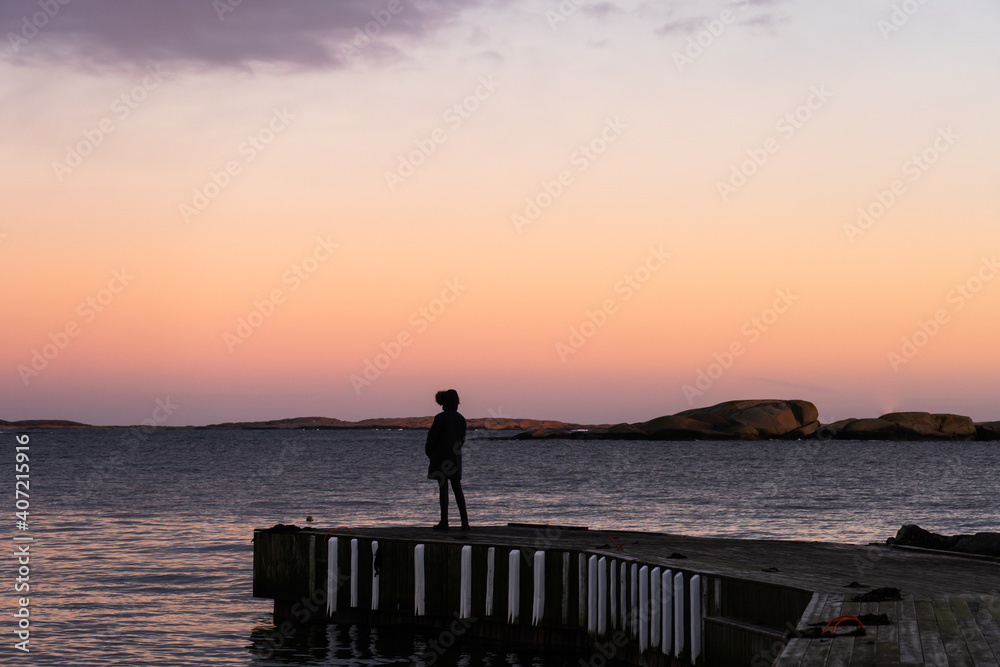 silhouette of a person standing on the pier at sunset in Norway silhouette of a person standing on the pier at sunset in Norway