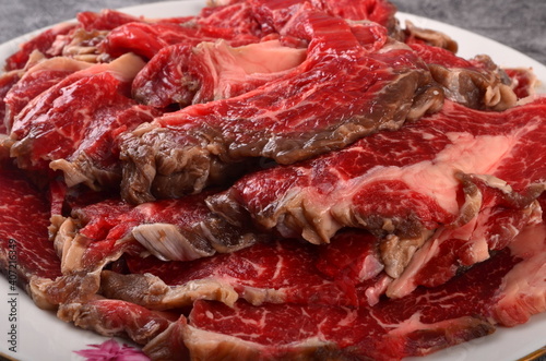 Thinly cut raw meat slices on a white plate, gray background