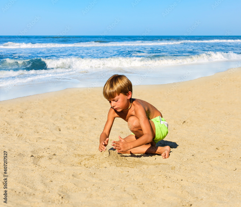 Child in bathing suit playing on the sand at the beach on a sunny day. In the background the beach and the ocean waves. Child in bathing suit playing on the sand at the beach on a sunny day. In the background the beach and the ocean waves.
