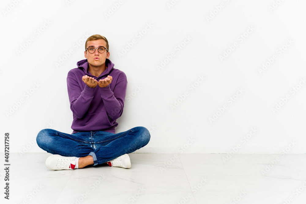 Young caucasian man sitting on the floor folding lips and holding palms to send air kiss. Young caucasian man sitting on the floor folding lips and holding palms to send air kiss.