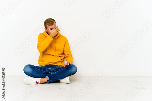 Young caucasian man sitting on the floor having a head ache, touching front of the face.