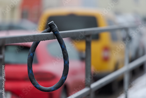 Thick round bike lock covered in white frost hanging on metal handrail in city with cars in background without bike