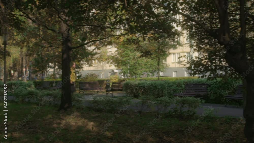 Male courier delivers an online order, moving on a skateboard, through a sunny park densely planted with trees and bushes. Pan camera movement. Male courier delivers an online order, moving on a skateboard, through a sunny park densely planted with trees and bushes. Pan camera movement.