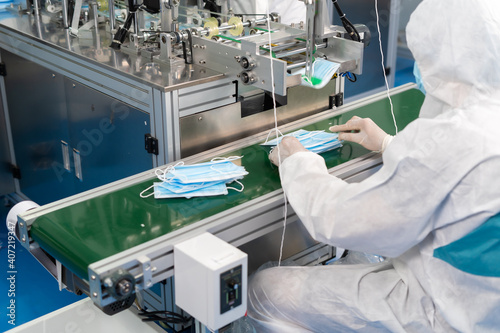 Caucasian Man worker inspecting the quality of the mask factory to in face mask production line factory. Surgical Face mask production, industry factory and people concept. indoors