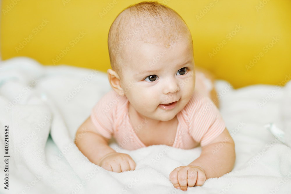 Adorable baby in sunny bedroom. Newborn baby is resting in bed with a warm soft blanket. Family morning at home. Smiling child looking at camera.