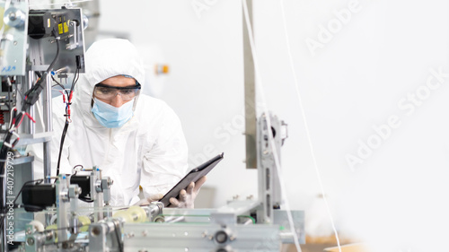 Professional engineering man in sterile cloths and face mask working and control machine in surgical mask factory. industry factory and people concept. indoors