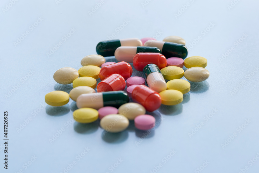 Colorful pills and capsules isolated on a blue background. Medical health or drugs addiction concept.