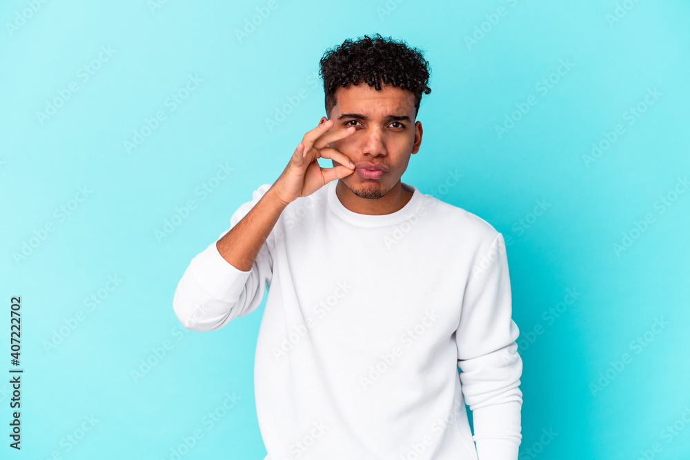 Young african american curly man isolated on blue with fingers on lips keeping a secret. Young african american curly man isolated on blue with fingers on lips keeping a secret.