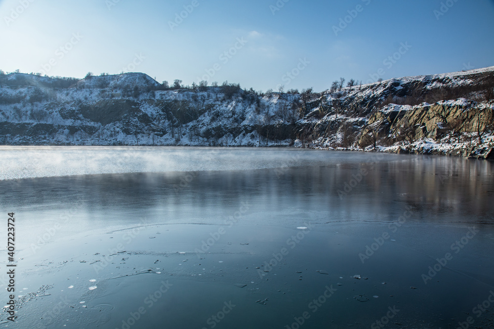 The weather is very cold. Steam rises above the water of a flooded quarry. A natural phenomenon. Winter. Walk on a sunny frosty day. Industrial tourism. Kryvyi Rih, Ukraine.