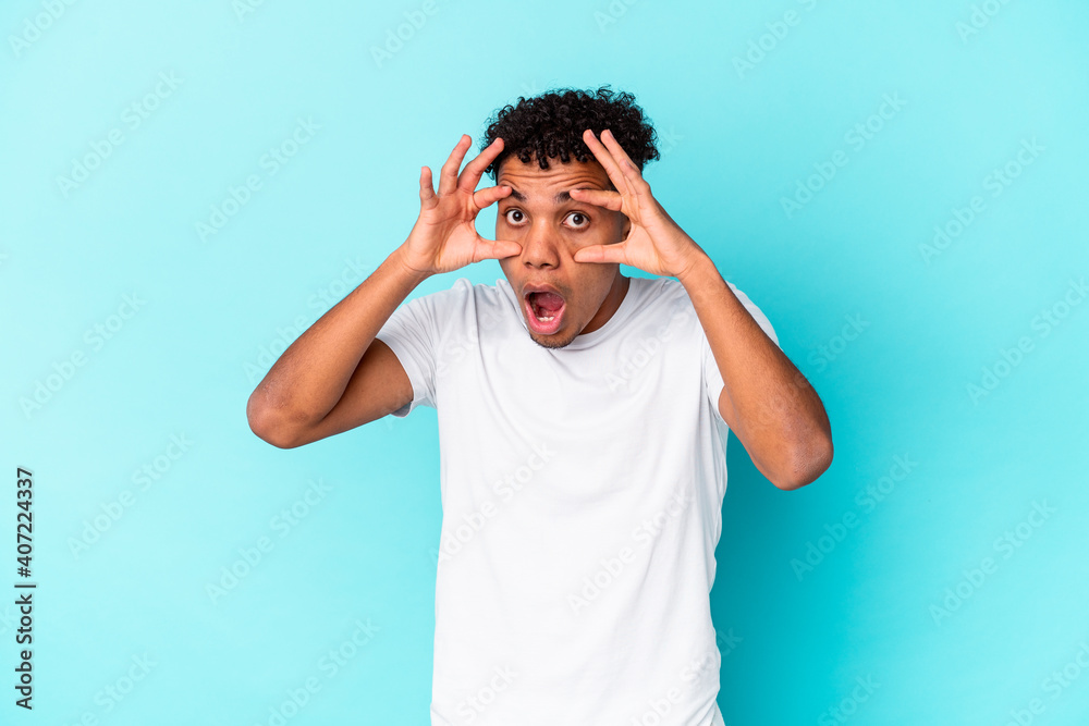 Fototapeta premium Young african american curly man isolated on blue keeping eyes opened to find a success opportunity.