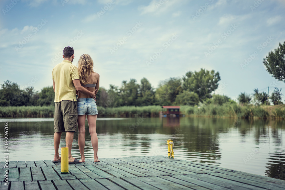 Beautiful young and handsome couple outdoors enjoying summertime in nature next to river lake. Man hugging woman. Love is forever