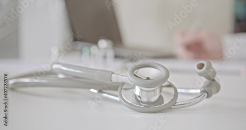 Stethoscope on a table in a physician examination room. Doctor inspects liquid medicine ampule, records patient examine results and summarize medical expense for claiming insurance. Healthcare concept