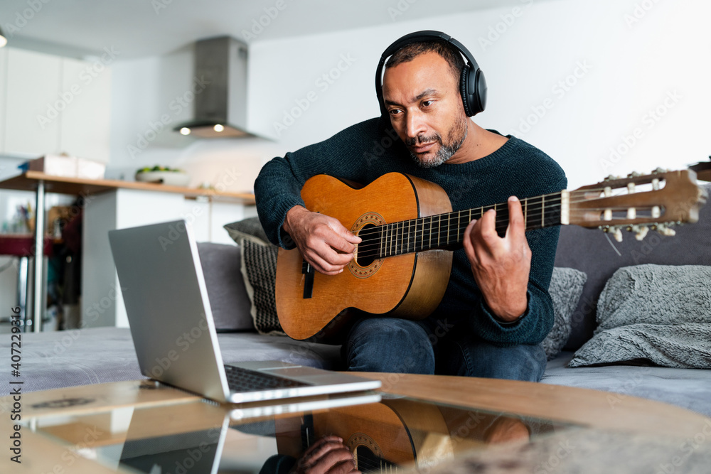 Obraz premium Relaxed man playing the guitar at home and using a laptop
