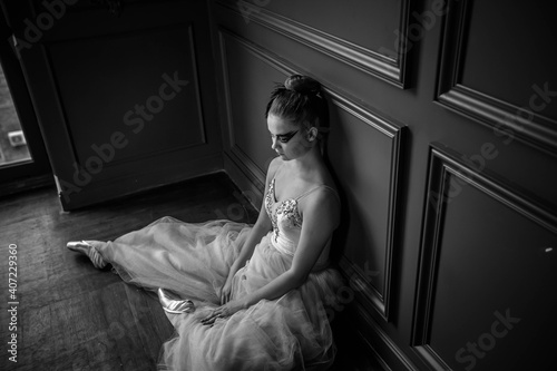 Young dancer sitting in a dance studio near the wall and resting. Black and white photo