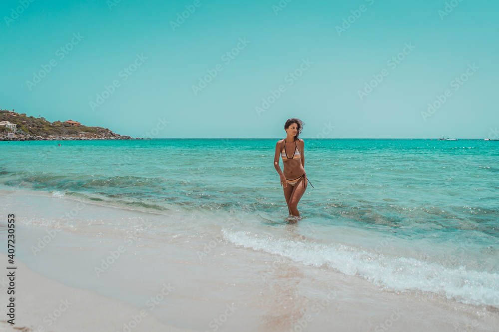 Beautiful young sexy female in bikini on vacation. Enjoying summer time on gorgeous sandy beach with beautiful sea.