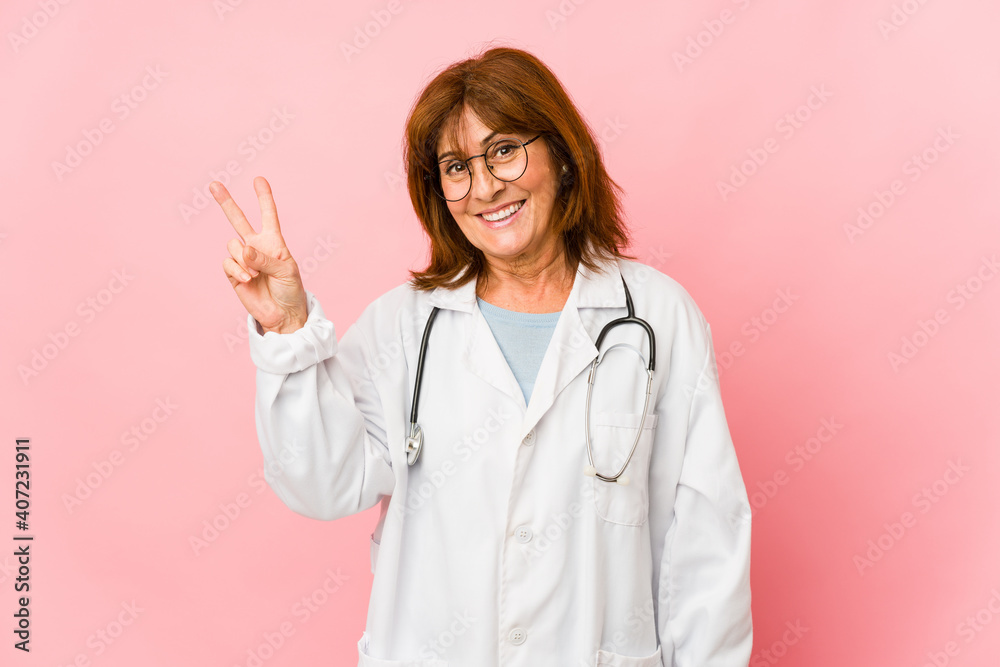Middle age caucasian doctor woman isolated joyful and carefree showing a peace symbol with fingers. Middle age caucasian doctor woman isolated joyful and carefree showing a peace symbol with fingers.