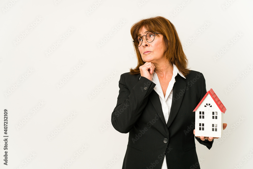 Middle aged real estate agent holding a house model isolated looking sideways with doubtful and skeptical expression. Middle aged real estate agent holding a house model isolated looking sideways with doubtful and skeptical expression.