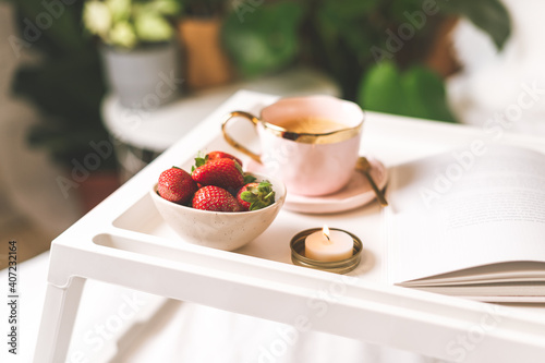  Breakfast in bed. Heart shaped white plate with fresh strawberries  cup of coffee  book and plants flowers. Still life composition. Mother  Valentine day concept.