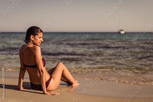 Beautiful young woman in bikini on vacation swimming in sea and enjoying in sand beach. Happy female enjoying summer time holiday on beach.