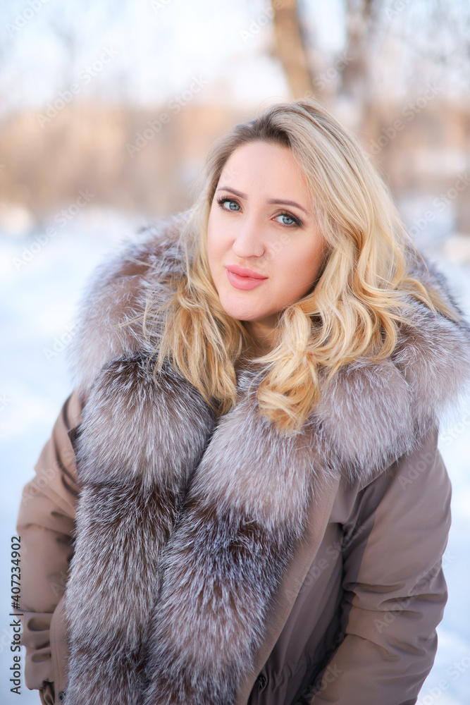 a beautiful blonde in a fur coat with a fur collar stands in a winter park a beautiful blonde in a fur coat with a fur collar stands in a winter park