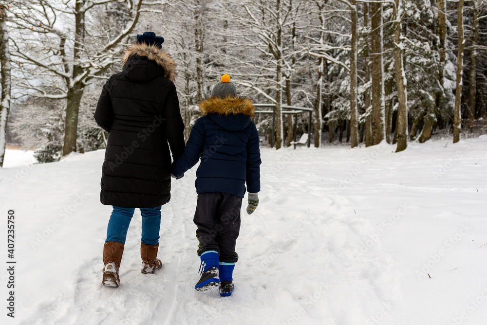 Mother and son walking together on a forest track in winter time.