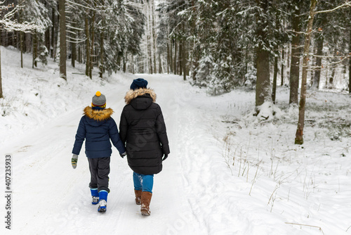 Mother and son walking together on a forest track in winter time.