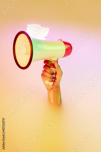 News, shouting, anouncement. Close up female hand gesturing from the milk bath with soft white glowing in neon light. Copyspace for advertising. Holding megaphone, rupor. Modern neoned colors. photo