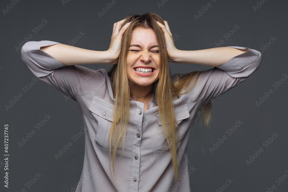 Young attractive woman in a blouse on a gray background, angry, annoyed woman holds her hand behind her head. Concept of emotional people, nerves, irritation Young attractive woman in a blouse on a gray background, angry, annoyed woman holds her hand behind her head. Concept of emotional people, nerves, irritation