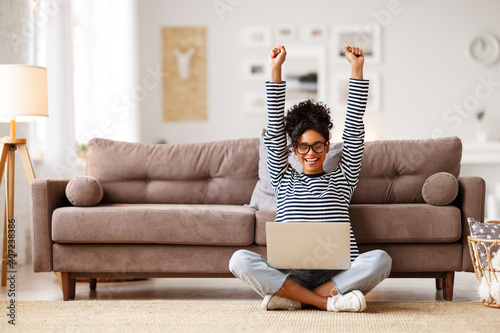 Fototapeta Glad woman celebrating good news while working on laptop at home