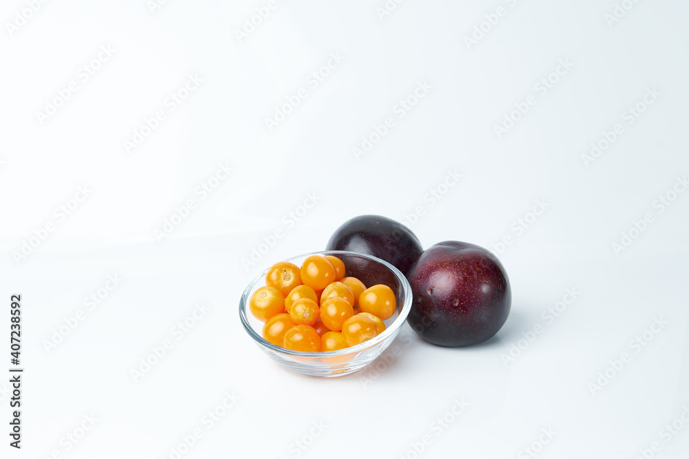 Glass container carrying cape gooseberries and next to it two juicy plums. Tropical fruits. Glass container carrying cape gooseberries and next to it two juicy plums. Tropical fruits.