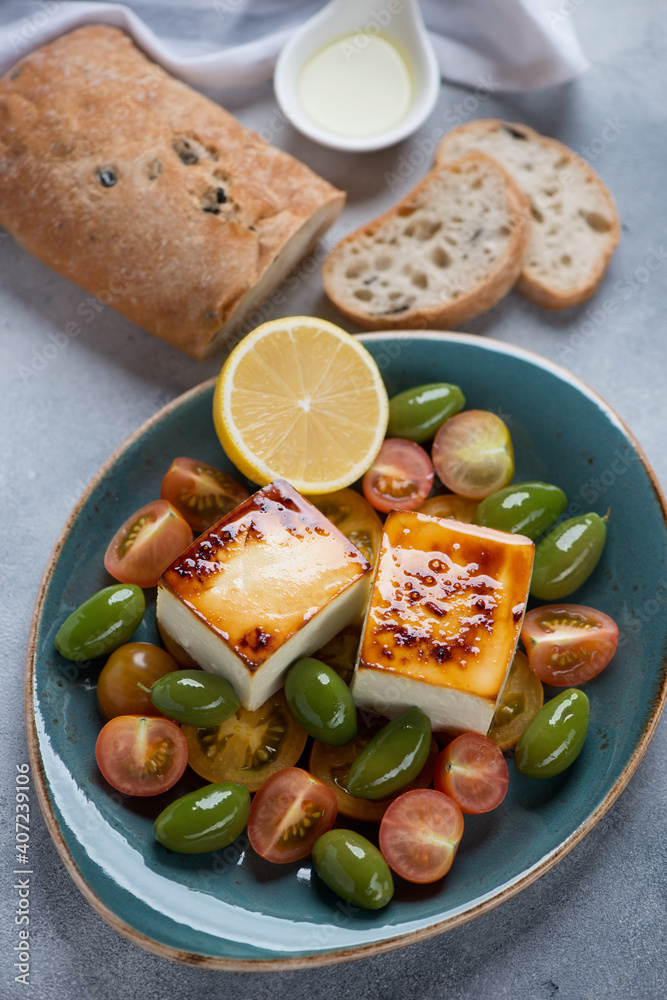 Turquoise plate with baked feta, tomatoes, green olives, ciabatta bread and olive oil, vertical shot Turquoise plate with baked feta, tomatoes, green olives, ciabatta bread and olive oil, vertical shot