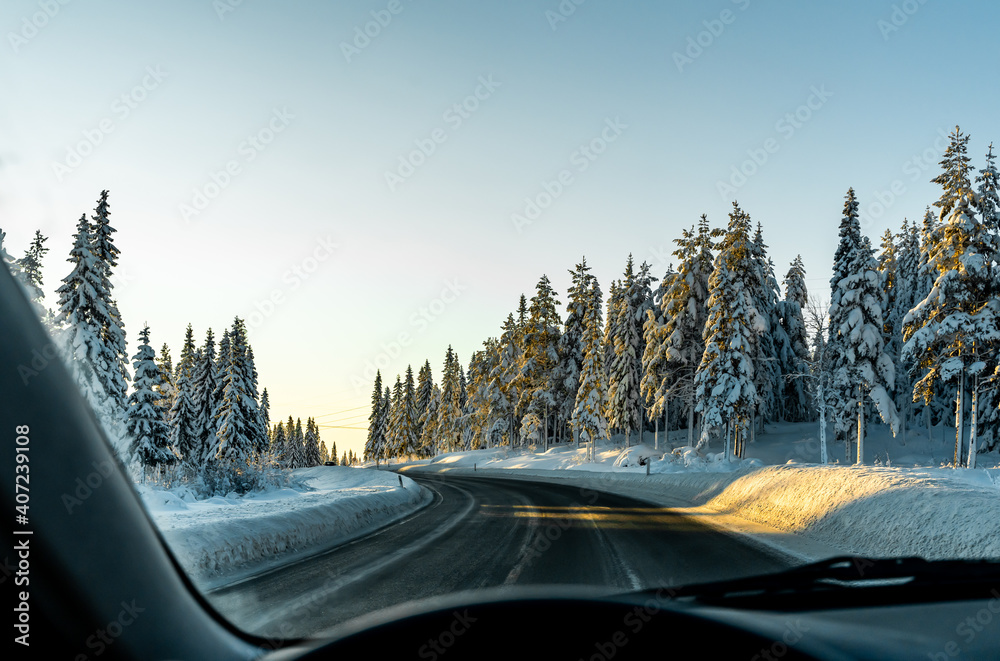 Fototapeta Driving along a slippery icy highway in a winter woodland. Drivers perspective, blurred foreground.