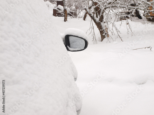 Car mirror of a snow-covered car against the backdrop of a snow-covered garden.