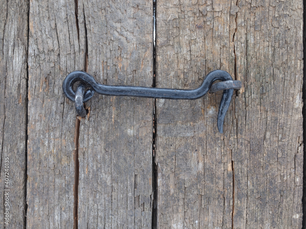 Black metal hook on a wooden door made from old spruce boards.