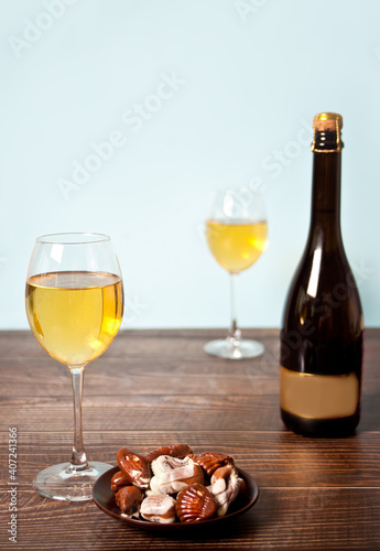 Glasses of champagne or white grape wine with plate of chocolates and bottle on the background on the wooden table.