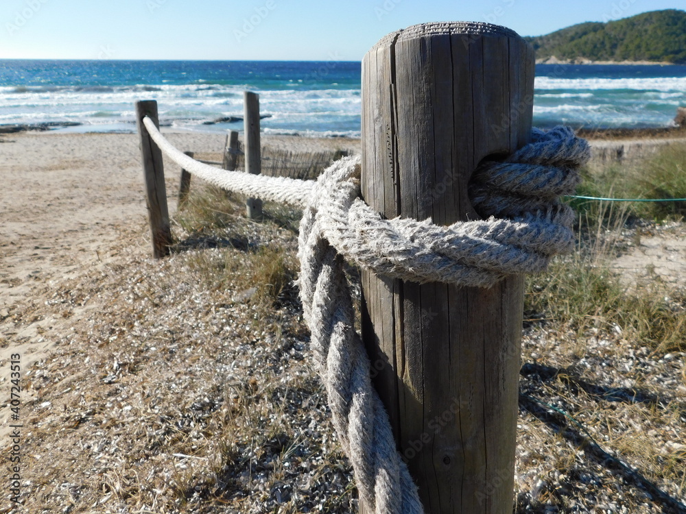 A rope attached to a wooden stick. A beach and the sea on the background