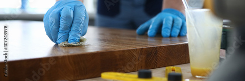 A carpenter in a workshop polishes a wooden surface. Man in gloves varnishes a board