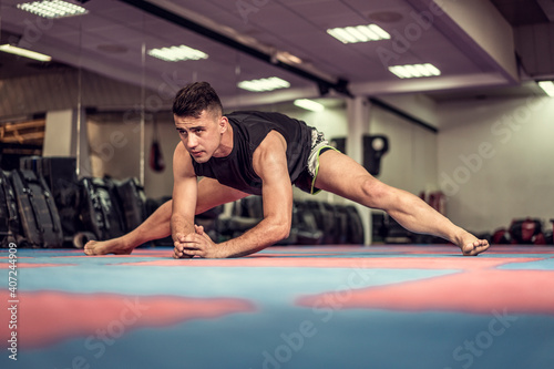 Fototapeta Naklejka Na Ścianę i Meble -  Young handsome kick boxer training hard, stretching and preparing. Fighter working out at gym