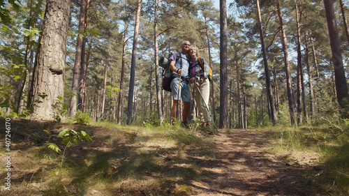 Happy couple seniors on hike with trekking poles standing in forest enjoying beautiful landscape