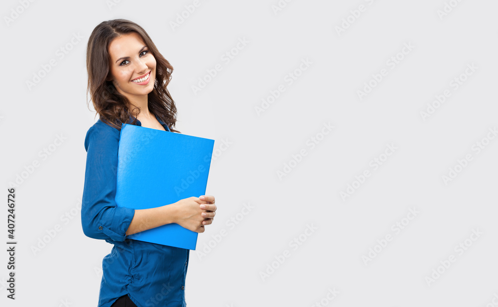 Portrait of happy smiling brunette businesswoman with blue folder, with blank copy space area for slogan or text, posing at studio against grey background Portrait of happy smiling brunette businesswoman with blue folder, with blank copy space area for slogan or text, posing at studio against grey background