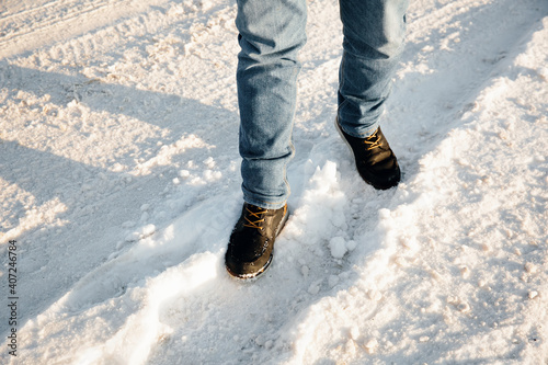 Man stands on a snowy road. Male legs in jeans and boots, close-up. Selective focus.