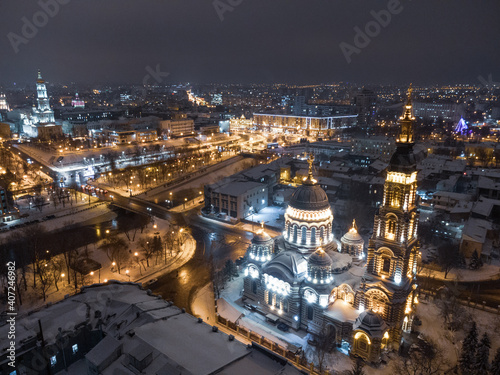 Holy Annunciation Cathedral illuminated in winter snowy night lights. Aerial view Kharkiv city orthodox church on riverbank, Ukraine. Side view from air.