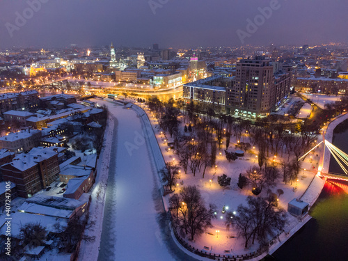 Winter evening illuminated city aerial landscape with frozen snowy river. Lopan embankment, Skver Strilka, Dormition Cathedral, Serhiivskyi Maidan in Kharkiv, Ukraine photo