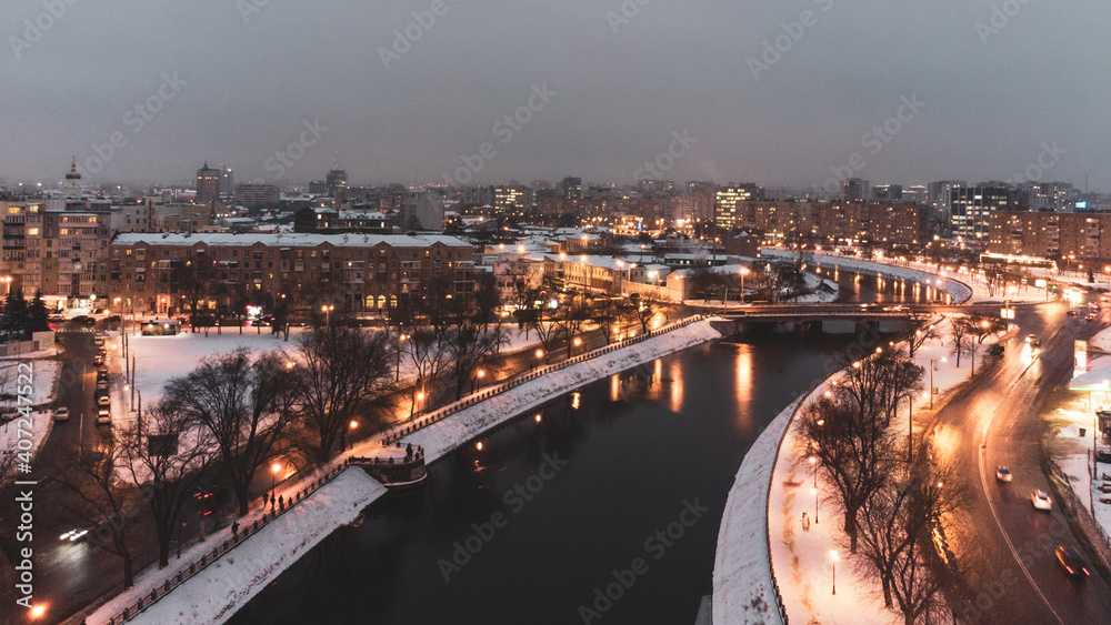 Illuminated evening riverbank with lights reflection in dark water near Skver Strilka in Kharkiv city center. Winter aerial colorful color graded photo