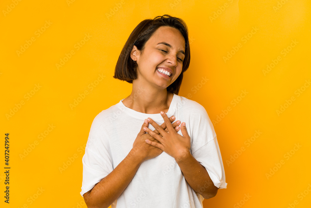 Young hispanic woman isolated on yellow laughing keeping hands on heart, concept of happiness. Young hispanic woman isolated on yellow laughing keeping hands on heart, concept of happiness.