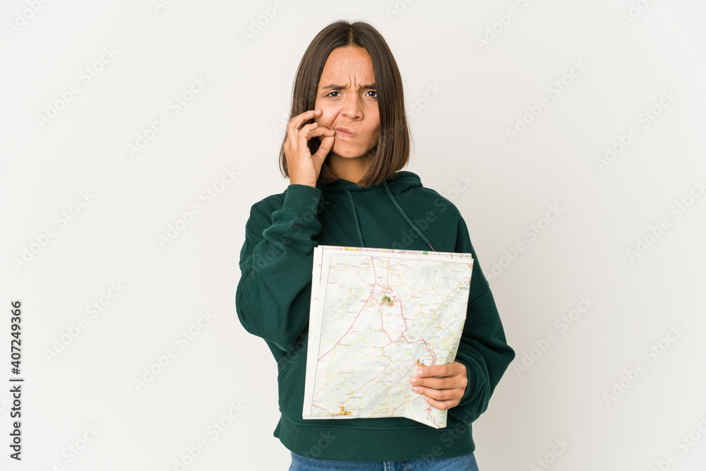 Fototapeta premium Young hispanic traveler woman holding a map with fingers on lips keeping a secret.