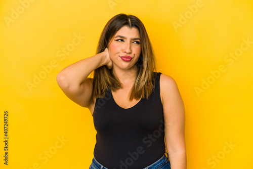 Young indian woman isolated on yellow background touching back of head, thinking and making a choice.