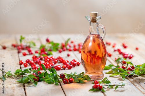 Bottle of rosehip oil on wooden palette with berries around. Clear oil fluid from sweet red fruit in jar with cork. Therapy with alternative medicine.
