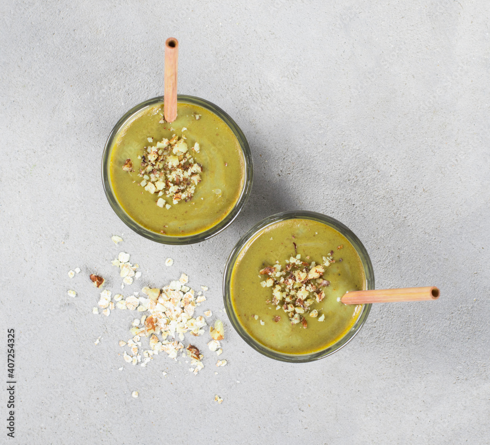 Vegan cocktail, smoothie made with oatmeal, walnuts and green matcha tea in a jar with bamboo straws on a light gray background top view 